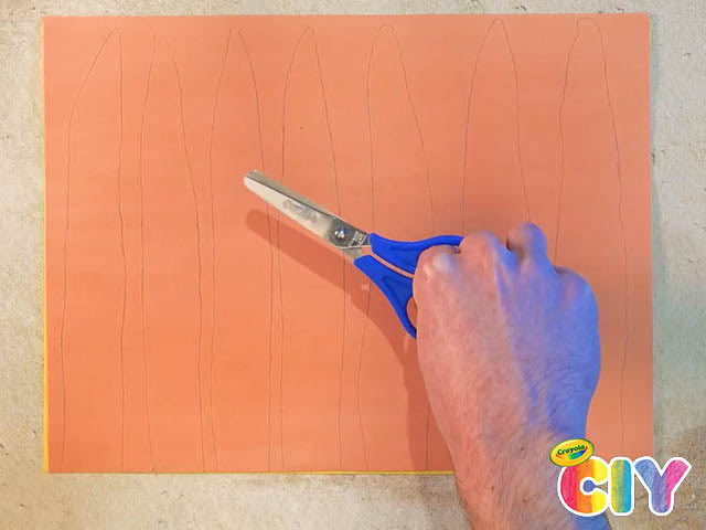 Hand holding scissor over orange construction paper