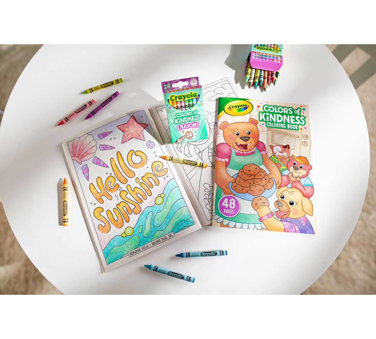 Colors of Kindness Coloring Book on table open to Hello Sunshine coloring page and surrounded by Colors of Kindness crayons.